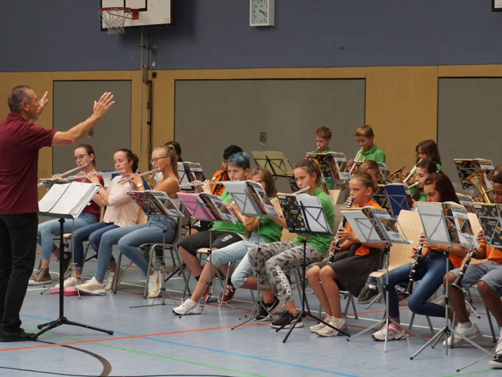 Person begrüßt das Orchester mit erhobener Hand.
